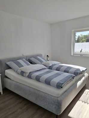 A bedroom with a bed, pillows, a nightstand, a lamp, and a window with a view of trees. - Apartment 'Kleine Schwalbe' with Private Terrace and Wi-Fi (Rechtsupweg)