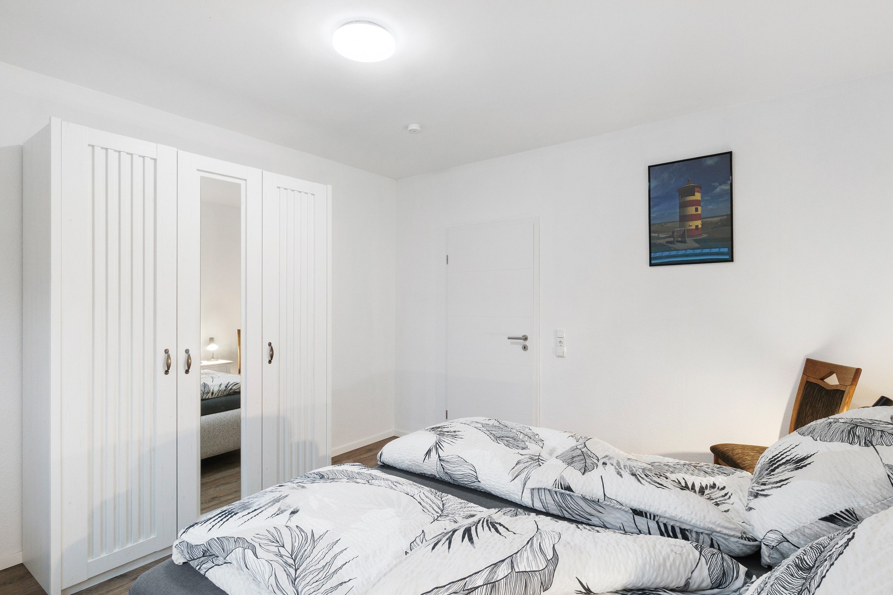 Ein Schlafzimmer mit einem Bett, einem Kleiderschrank, einem Gemälde und einer Tür.