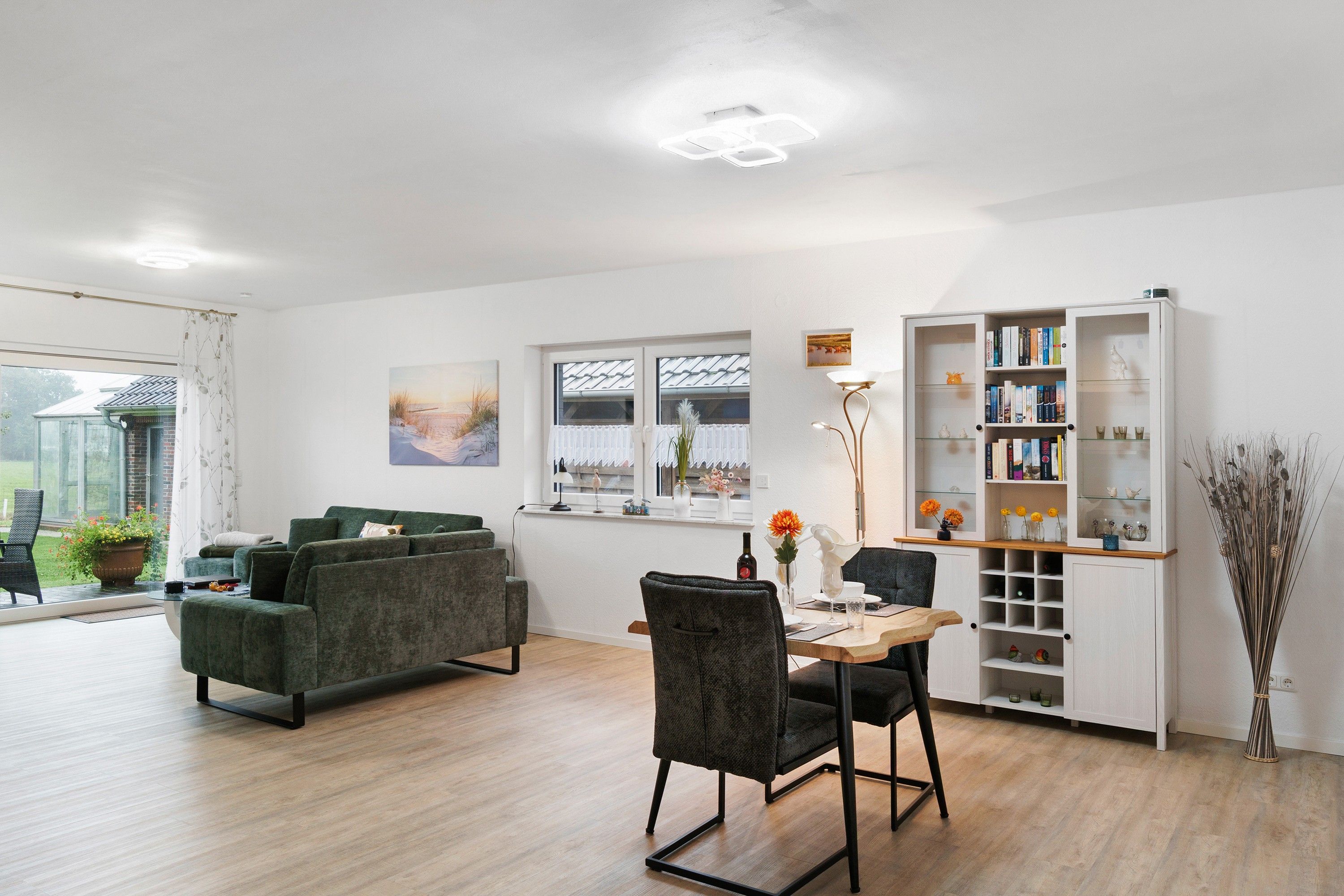 A modern living room with a dining area, a bookshelf, and a view of the outdoors.