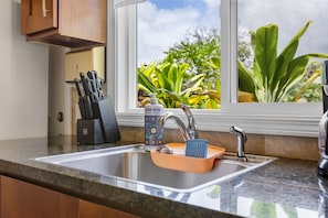 A kitchen with a granite countertop, stainless steel sink, and a window with a view of greenery.