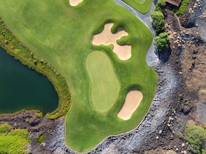 An aerial view of a golf course with sand bunkers, a water body, and a building.