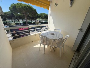 Ein Balkon mit Tisch und Stühlen, ein gelbes Markisenvorzelt und Blick auf parkende Autos und Bäume.