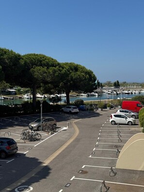 A parking lot with cars and bicycles, a marina with boats, and a clear blue sky. - Le Balcon du Chenal, Sleeps 4, Boat View (Le Grau-du-Roi)