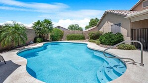 Ein Pool mit gewölbter Kante, umgeben von einer Betonplattform und Palmen.