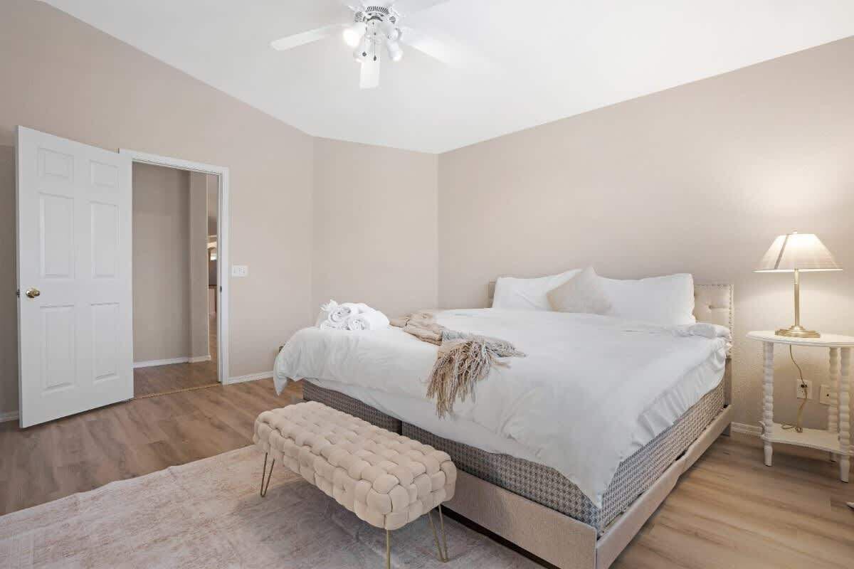 Een slaapkamer met een bed, een bankje, een nachtkastje, een lamp en een plafondventilator.