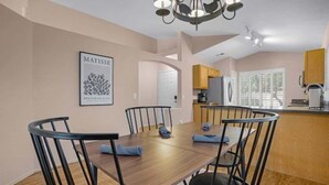 Ein Essbereich mit Holztisch und -stühlen, einer Chandelier und einer Küche im Hintergrund.