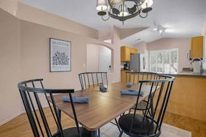 Een eetruimte met een houten tafel en stoelen, een kroonluchter en een keuken op de achtergrond.