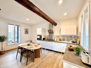 A modern kitchen with a central island, white cabinetry, and a wooden ceiling beam. - La Romaine, 2 guests, city centre, king-size bed (Nîmes)