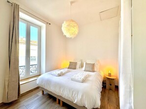 A bedroom with a bed, two bedside tables, a hanging light fixture, and a window with curtains. - La Romaine, 2 guests, city centre, king-size bed (Nîmes)
