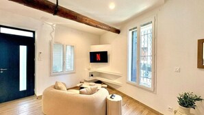 Una sala de estar moderna con un sofá modular, un televisor montado en la pared y un amplio ventanal con persianas.