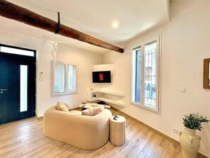 A modern living room with a sectional sofa, a TV mounted on the wall, and a large window with blinds. - La Romaine, 2 guests, city centre, king-size bed (Nîmes)