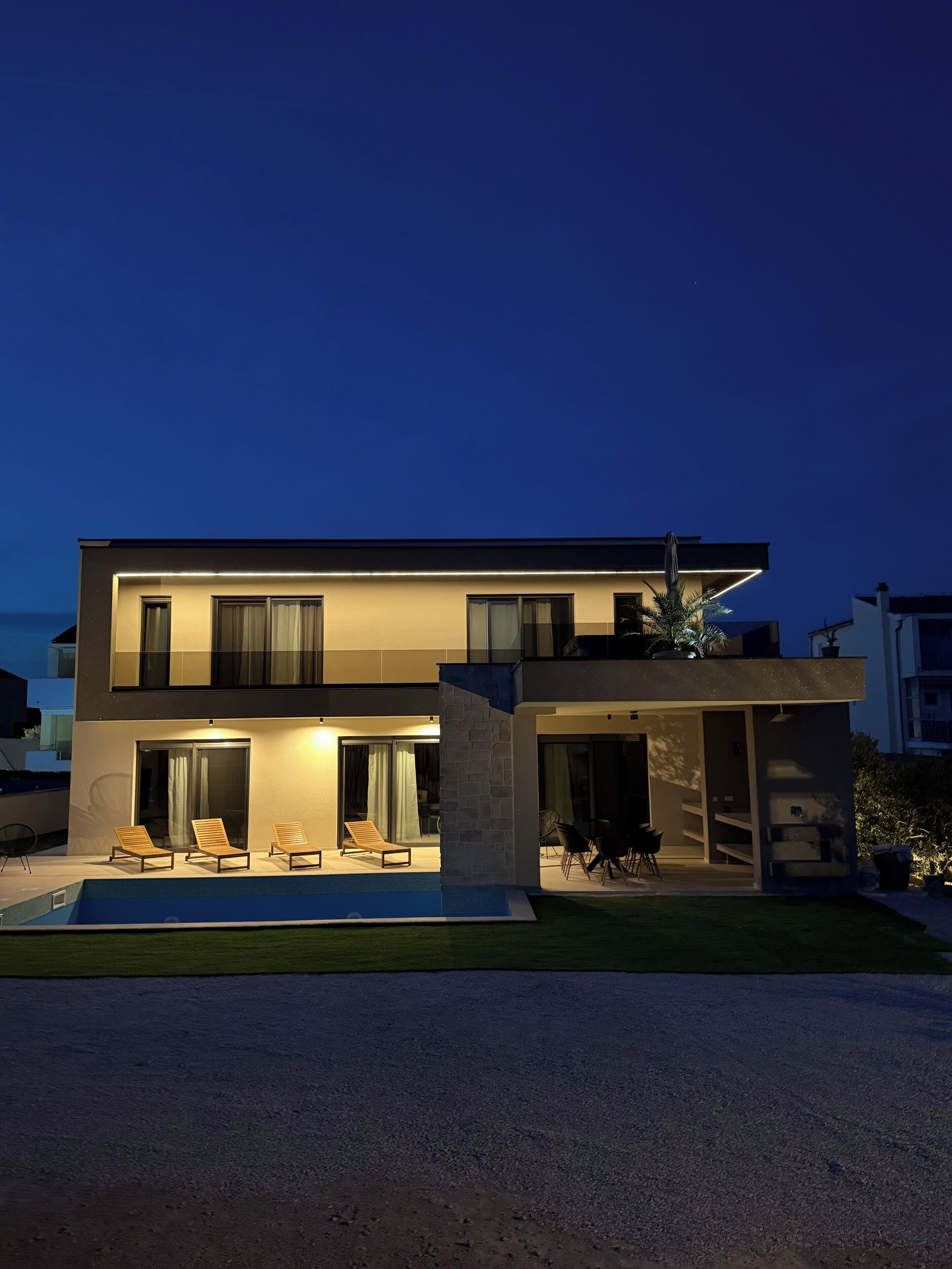 Una casa moderna de dos plantas con piscina, zona de estar exterior y un patio bien iluminado.