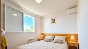 A bedroom with a large bed, a window, a radiator, a wall-mounted air conditioner, and a small bedside table with a lamp. - La cachette du mas, 4 guests, Pool in Calvisson (Calvisson)