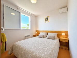A bedroom with a large bed, a window, a radiator, a wall-mounted air conditioner, and a small bedside table with a lamp. - La cachette du mas, 4 guests, Pool in Calvisson (Calvisson)