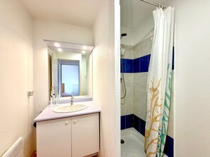 Uma casa de banho com lavatório, espelho e chuveiro.