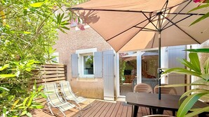 A wooden deck with a table and chairs, a large umbrella, and a window with shutters. - La cachette du mas, 4 guests, Pool in Calvisson (Calvisson)