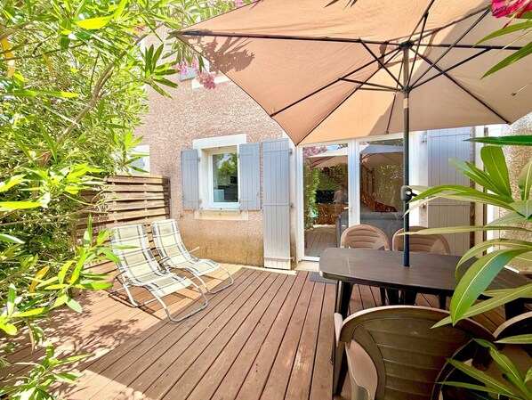 A wooden deck with a table and chairs, a large umbrella, and a window with shutters. - La cachette du mas, 4 guests, Pool in Calvisson (Calvisson)
