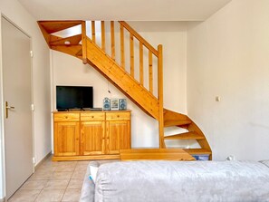 A room with a wooden staircase, a TV on a wooden cabinet, and a bed with a mattress. - La cachette du mas, 4 guests, Pool in Calvisson (Calvisson)