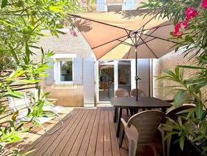 A wooden deck with a table and chairs, a large umbrella, and a building with windows and shutters. - La cachette du mas, 4 guests, Pool in Calvisson (Calvisson)