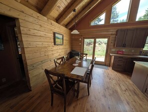 L’intérieur d’un chalet en bois comprend une table à manger, des chaises, un coin cuisine et une grande fenêtre.
