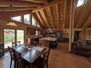 A spacious kitchen with wooden beams, a dining area with a table and chairs, and a cozy living room with a sofa. - River Valley Lodge - 79393 Brae Gate (Portola)