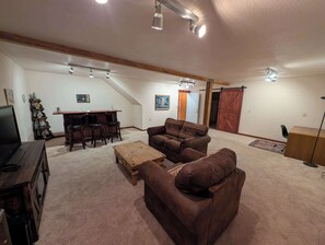 Un salon spacieux avec un plafond haut, un meuble de rangement en bois pour les appareils multimédias, un canapé, une table basse et un coin repas avec des tabourets de bar.