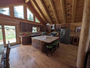 A spacious kitchen with wooden floors, a large island with stools, a refrigerator, and a microwave. - River Valley Lodge - 79393 Brae Gate (Portola)