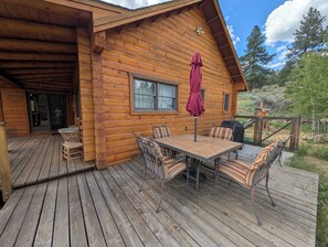 A wooden cabin with a deck, a table with chairs, and a covered patio area. - River Valley Lodge - 79393 Brae Gate (Portola)