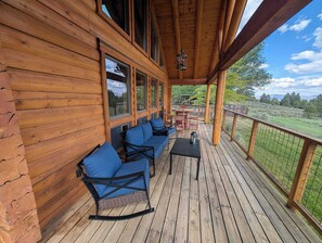A wooden deck with blue chairs and a table, overlooking a grassy landscape. - River Valley Lodge - 79393 Brae Gate (Portola)