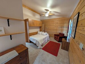 A compact room with a bed, a red rug, a wooden wardrobe, and a ceiling fan. - River Valley Lodge - 79393 Brae Gate (Portola)