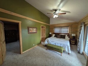 Une chambre à coucher avec un lit, un mur vert, un ventilateur de plafond et une fenêtre ornée de rideaux à motifs.