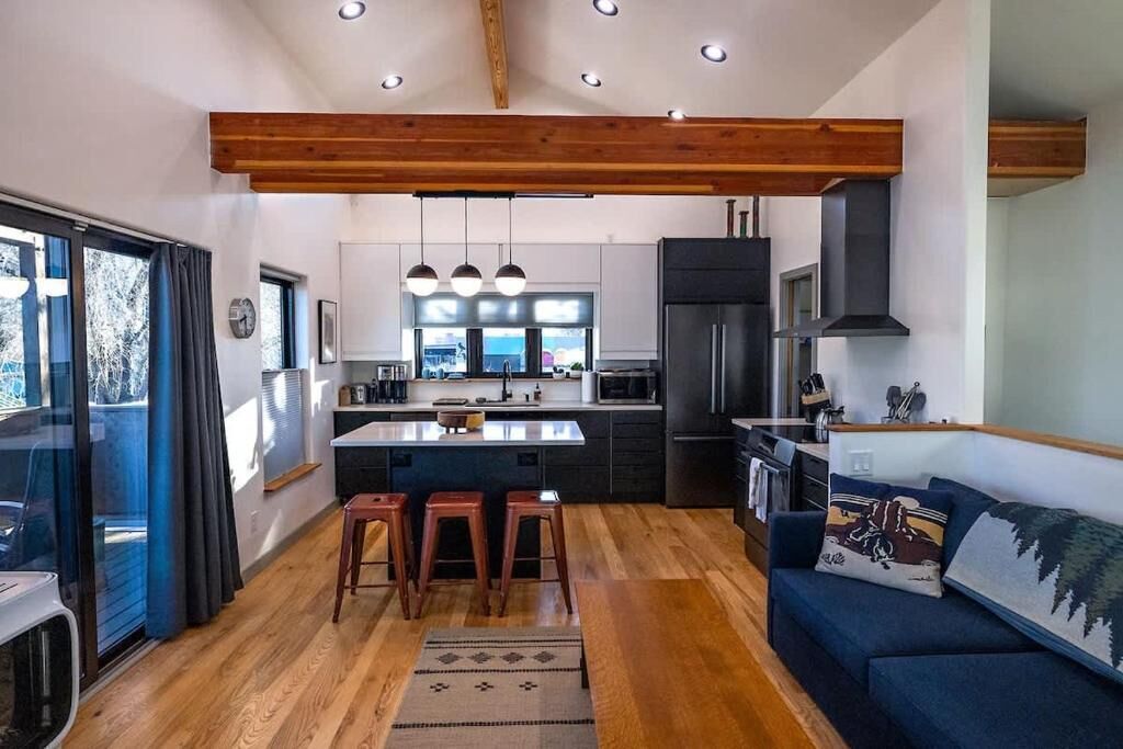 A modern kitchen with wooden beams, a central island, bar stools, and a dark refrigerator.