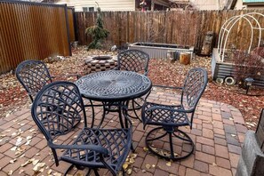 A patio with a round table and six chairs, surrounded by a wooden fence and a brick pathway. - NEW! Library House! AC/Grill/Near downtown. (Flagstaff)