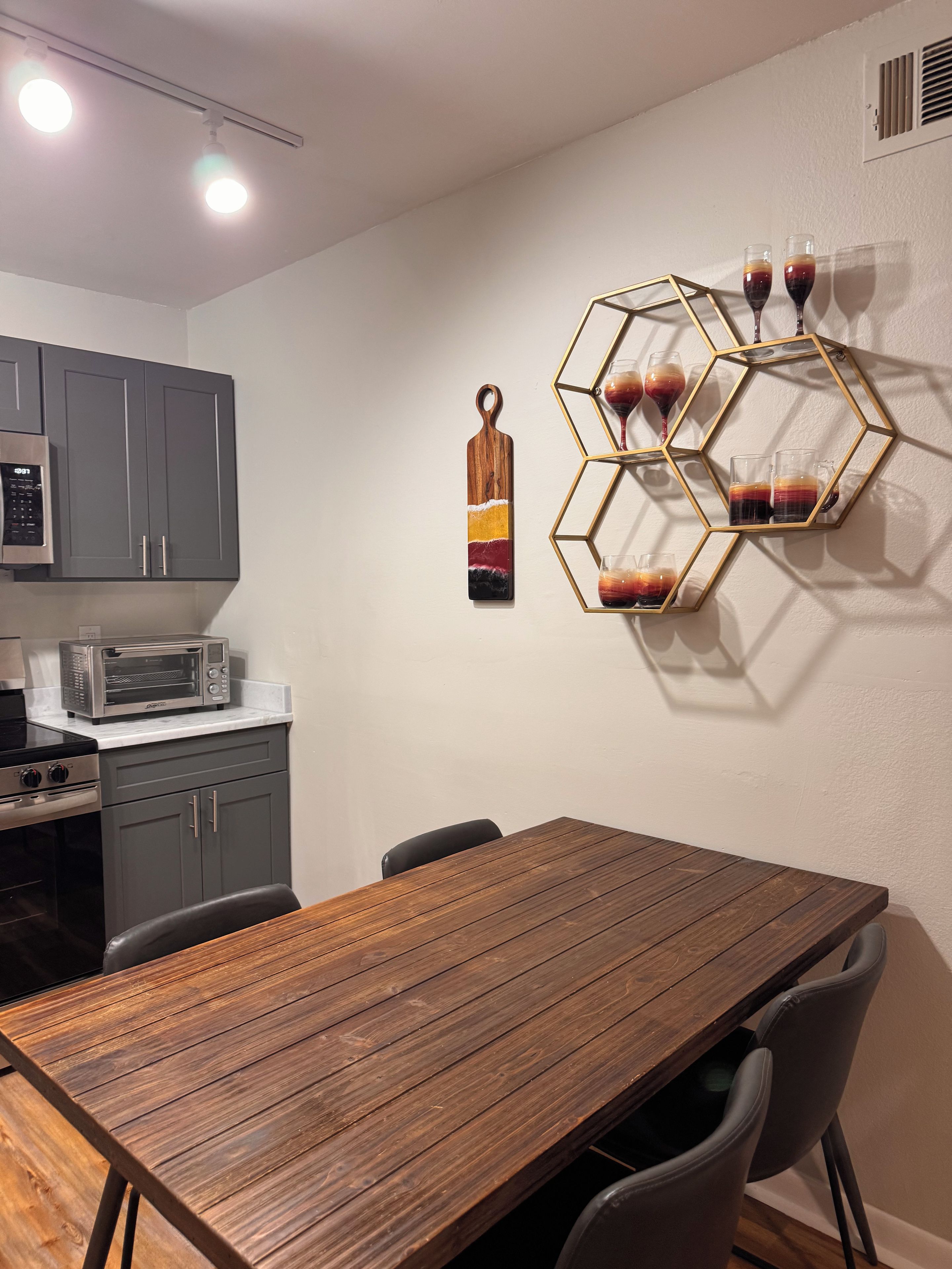 Eine moderne Küche mit grauen Schränken, einem Holztisch und einer sechseckigen Wanddekoration mit Gläsern.