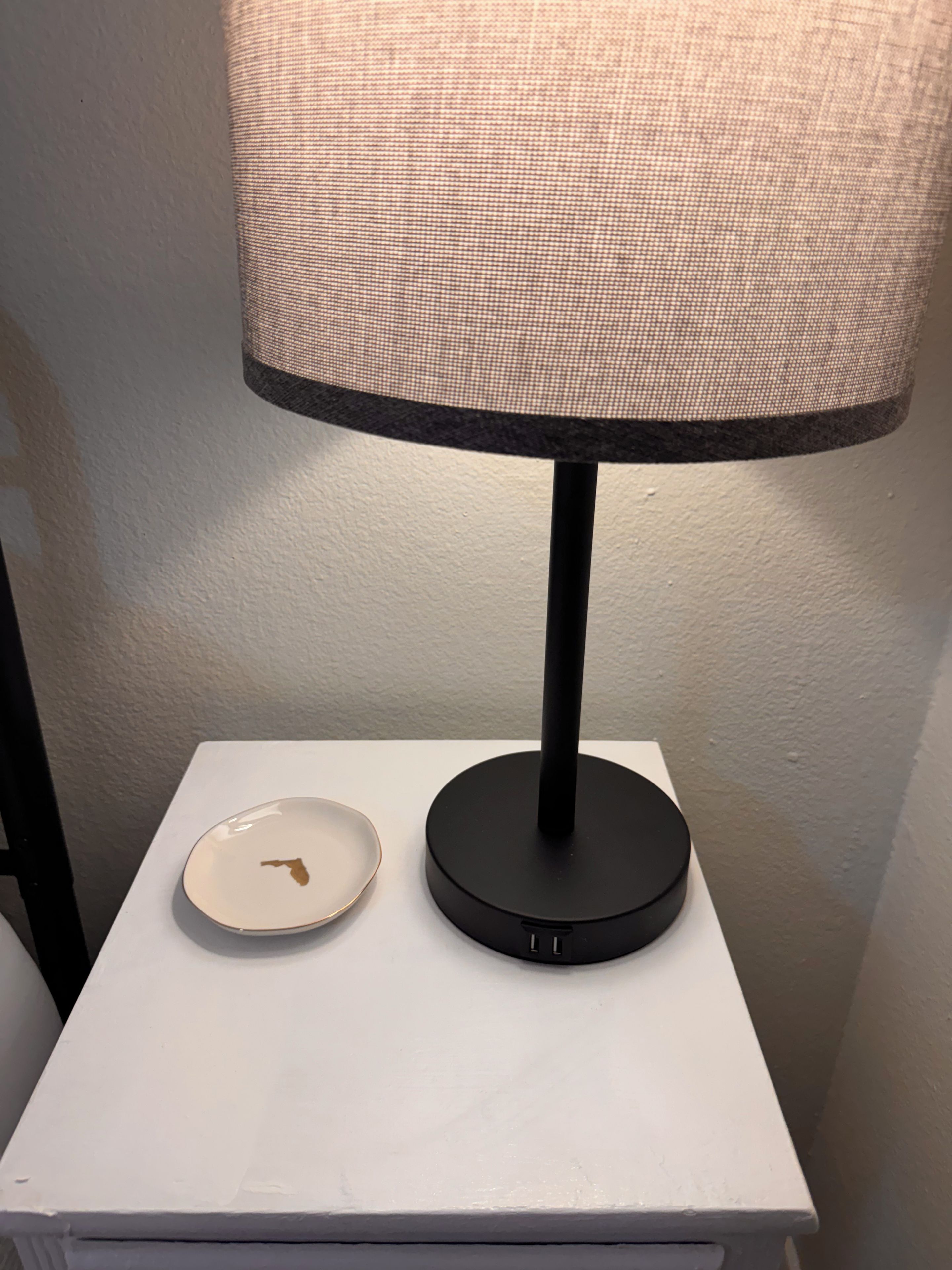 A white bedside table with a black lamp and a small white plate.