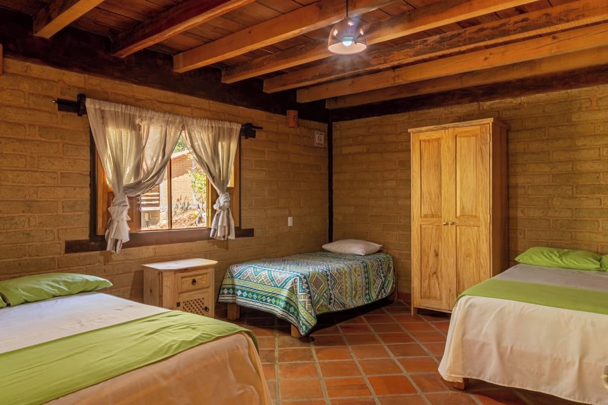 Une chambre avec deux lits, une armoire en bois, une fenêtre avec des rideaux et un plafond en bois.