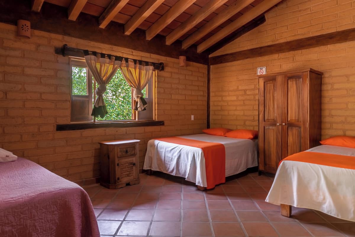 Une chambre avec deux lits, une armoire en bois, une fenêtre avec des rideaux et un mur en briques.