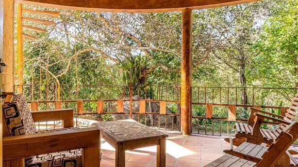 Una zona de estar al aire libre con mobiliario de madera y vista a árboles.