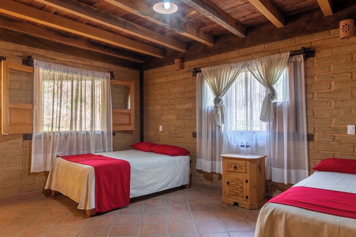 Une chambre avec deux lits, des poutres en bois au plafond, des murs en briques et une petite armoire en bois.