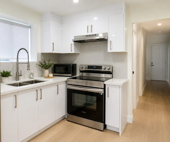 A modern kitchen with white cabinets, stainless steel appliances, and a wooden floor.