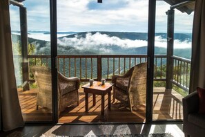 Un balcón con sillas de mimbre, una mesita y vistas a un paisaje montañoso.