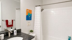 Een badkamer met een wit wastafel, spiegel en toilet, een douche met een witte douchegordijn, en een kleine potplant op het aanrecht.
