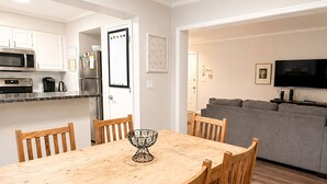 Een moderne keuken met witte kasten, roestvrijstalen apparatuur en een eethoek met een houten tafel en stoelen.