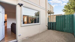 A residential building with a sliding glass door, a visible living room with a sofa, and a green fence. - -Cozy 2-Bedroom Retreat in Pacifica (Pacifica)