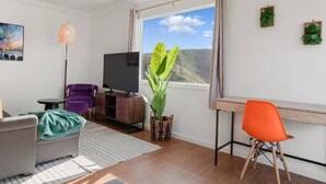 Una sala moderna con sofá, una silla, televisor, planta y escritorio con silla.