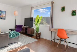 Un salon moderne comprenant un canapé, un fauteuil, un téléviseur, une plante et un bureau avec une chaise.