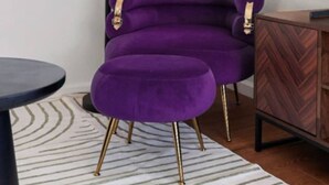 Una habitación con un sillón morado, un reposapiés a juego, una mesita auxiliar negra, un aparador de madera y un televisor grande en la pared.