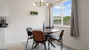 A dining area with a round table, four chairs, a chandelier, a window with curtains, and a kitchen area with cabinets and a stove. - +Tranquil 2BR with Coastal and Mountain Views (Pacifica)