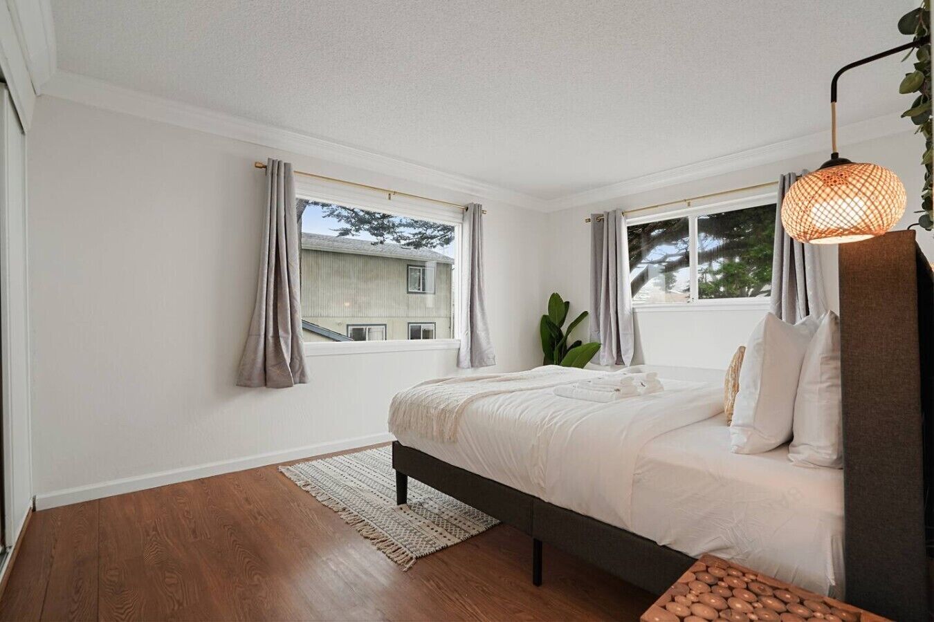 Un dormitorio con una cama, dos ventanas, una planta y una lámpara colgante.