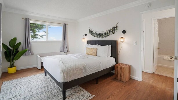 A bedroom with a bed, bedside tables, a potted plant, a window with curtains, and a door. - +Tranquil 2BR with Coastal and Mountain Views (Pacifica)